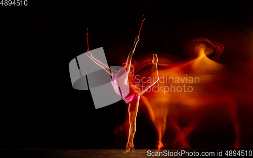 Image of Young flexible female gymnast isolated on black studio background in mixed light,