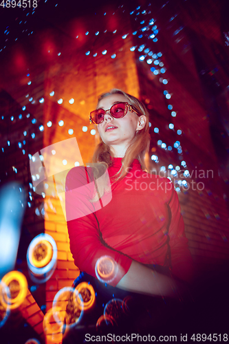 Image of Cinematic portrait of handsome young woman in neon lighted room, stylish musician