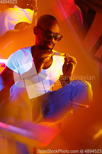 Image of Cinematic portrait of handsome young man in neon lighted room, stylish musician