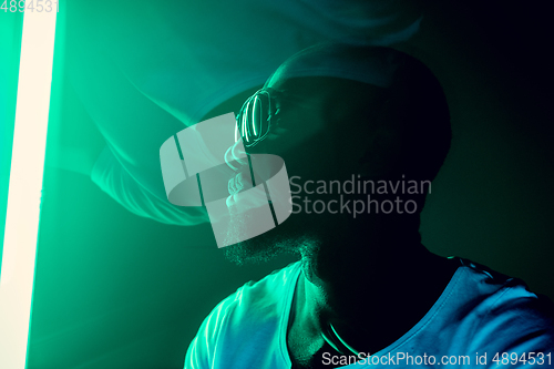 Image of Cinematic portrait of handsome young man in neon lighted room, stylish musician