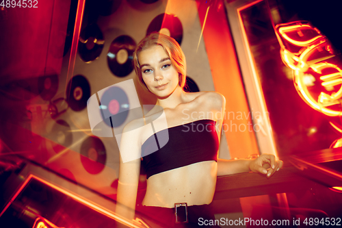 Image of Cinematic portrait of handsome young woman in neon lighted room, stylish musician