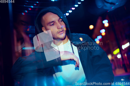 Image of Cinematic portrait of handsome young man in neon lighted room, stylish musician