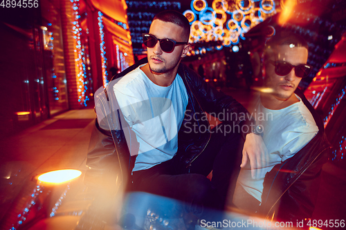 Image of Cinematic portrait of handsome young man in neon lighted room, stylish musician