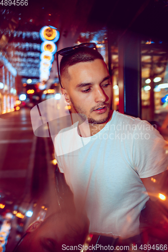 Image of Cinematic portrait of handsome young man in neon lighted room, stylish musician