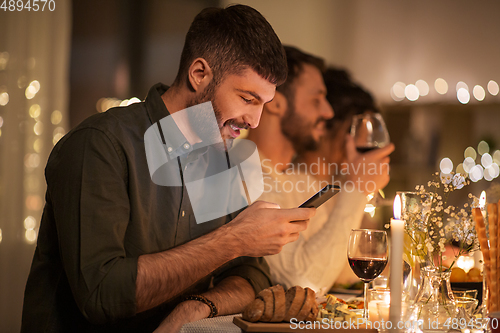 Image of man with smartphone at dinner party with friends