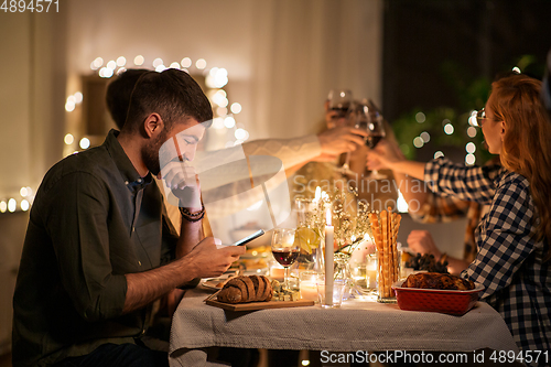 Image of man with smartphone at dinner party with friends
