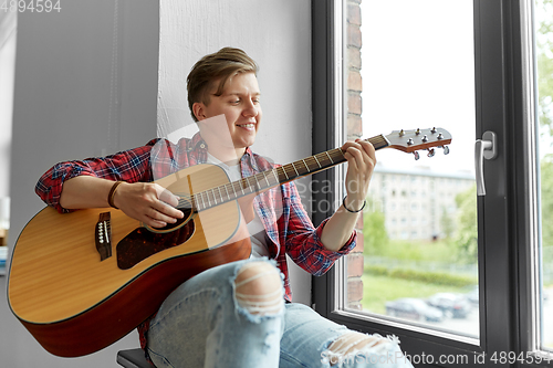 Image of young man playing guitar sitting on windowsill