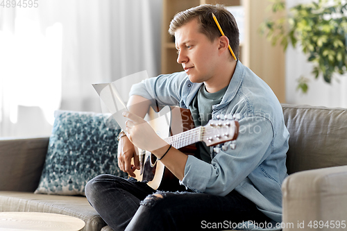 Image of young man with guitar and music book at home