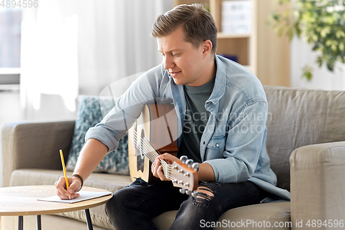 Image of man with guitar writing to music book at home