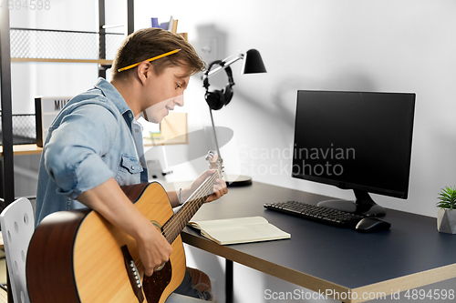 Image of young man with music book playing guitar at home