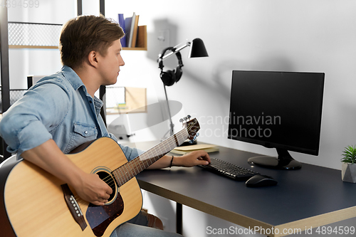 Image of young man with computer playing guitar at home