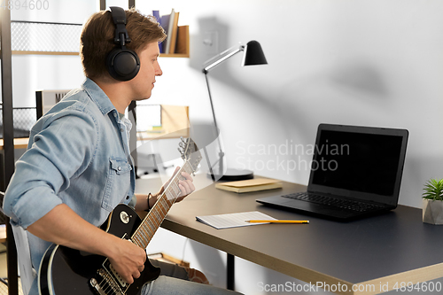 Image of man in headphones playing bass guitar at home