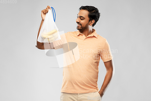 Image of happy man holding reusable string bag with bananas