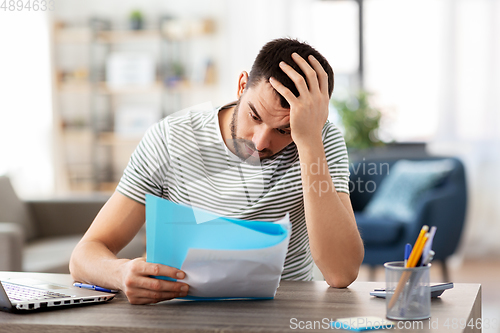 Image of man with papers and laptop working at home office