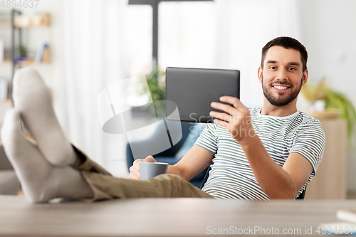 Image of man with tablet pc resting feet on table at home