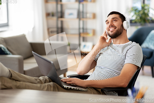 Image of happy man with laptop and headphones at home