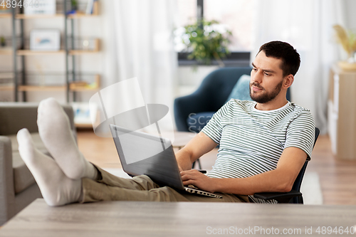 Image of man with laptop resting feet on table at home