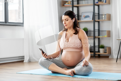 Image of pregnant woman with earphones doing yoga at home