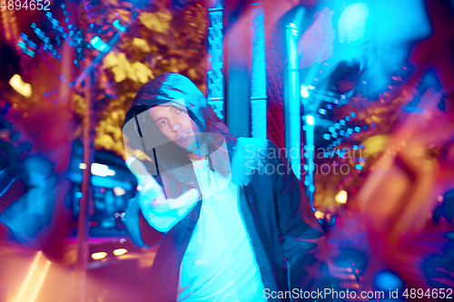 Image of Cinematic portrait of handsome young man in neon lighted room, stylish musician