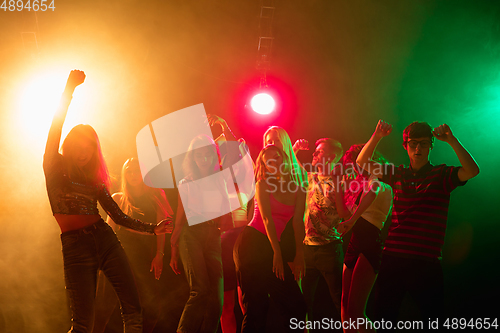 Image of A crowd of people in silhouette raises their hands on dancefloor on neon light background