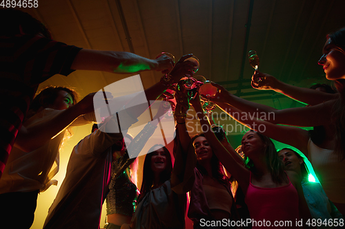 Image of A crowd of people in silhouette raises their hands on dancefloor on neon light background