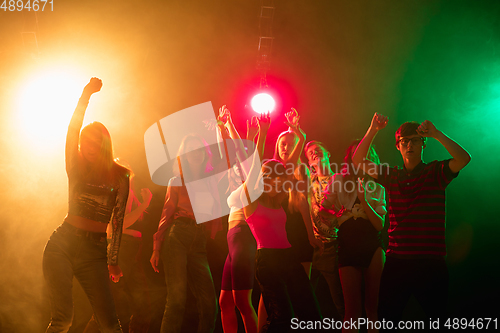 Image of A crowd of people in silhouette raises their hands on dancefloor on neon light background