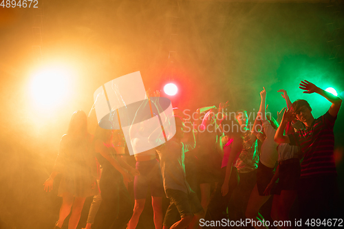 Image of A crowd of people in silhouette raises their hands on dancefloor on neon light background