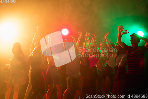 Image of A crowd of people in silhouette raises their hands on dancefloor on neon light background