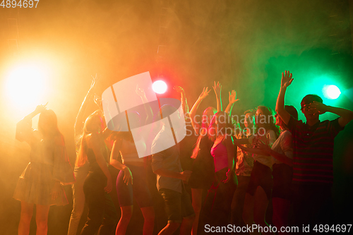 Image of A crowd of people in silhouette raises their hands on dancefloor on neon light background