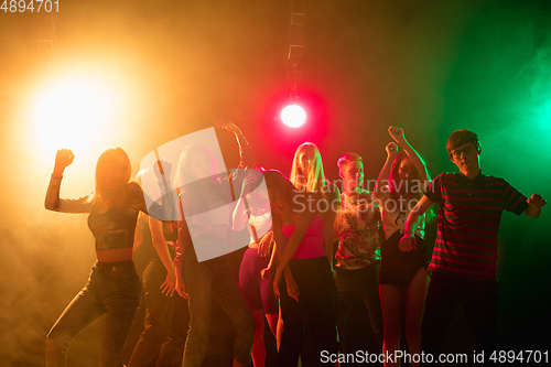 Image of A crowd of people in silhouette raises their hands on dancefloor on neon light background