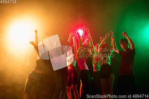 Image of A crowd of people in silhouette raises their hands on dancefloor on neon light background