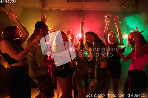 Image of A crowd of people in silhouette raises their hands on dancefloor on neon light background