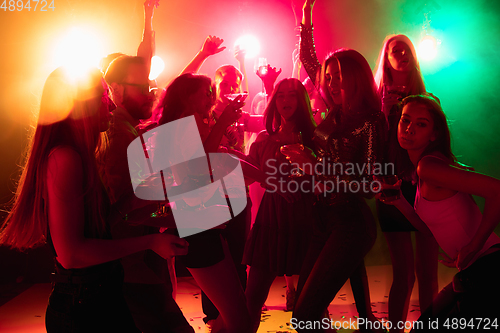 Image of A crowd of people in silhouette raises their hands on dancefloor on neon light background