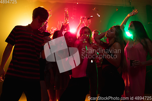 Image of A crowd of people in silhouette raises their hands on dancefloor on neon light background