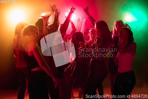 Image of A crowd of people in silhouette raises their hands on dancefloor on neon light background