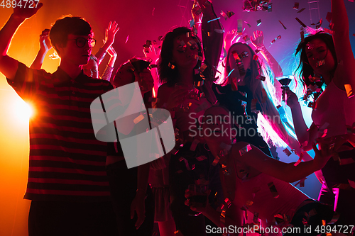 Image of A crowd of people in silhouette raises their hands on dancefloor on neon light background