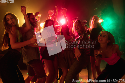 Image of A crowd of people in silhouette raises their hands on dancefloor on neon light background