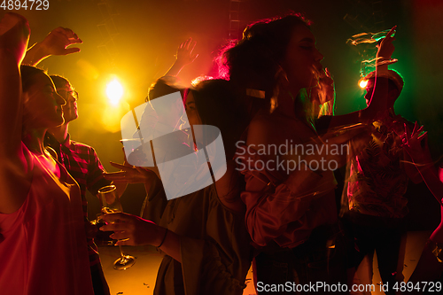 Image of A crowd of people in silhouette raises their hands on dancefloor on neon light background