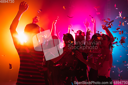 Image of A crowd of people in silhouette raises their hands on dancefloor on neon light background