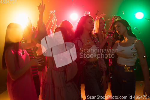 Image of A crowd of people in silhouette raises their hands on dancefloor on neon light background