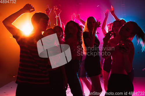 Image of A crowd of people in silhouette raises their hands on dancefloor on neon light background