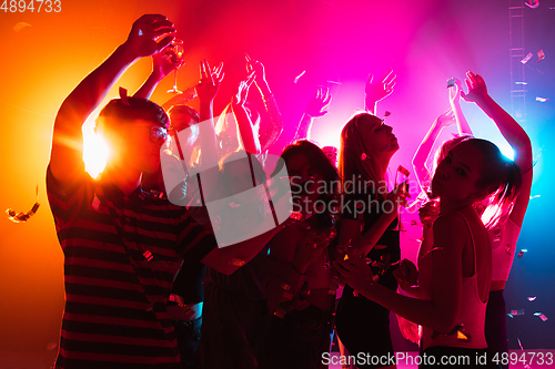 Image of A crowd of people in silhouette raises their hands on dancefloor on neon light background