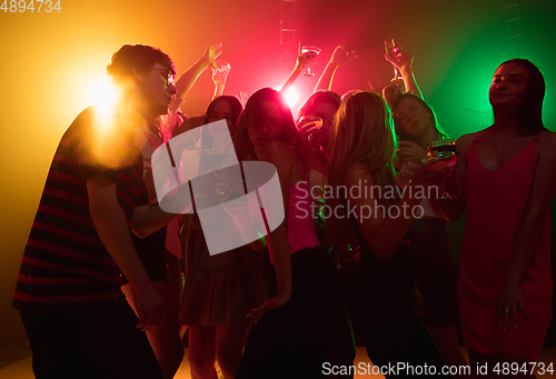 Image of A crowd of people in silhouette raises their hands on dancefloor on neon light background