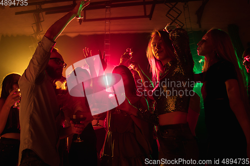 Image of A crowd of people in silhouette raises their hands on dancefloor on neon light background