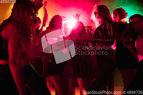 Image of A crowd of people in silhouette raises their hands on dancefloor on neon light background