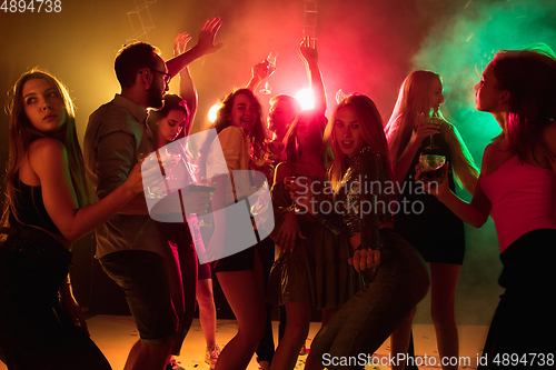 Image of A crowd of people in silhouette raises their hands on dancefloor on neon light background