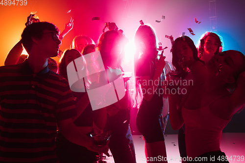 Image of A crowd of people in silhouette raises their hands on dancefloor on neon light background