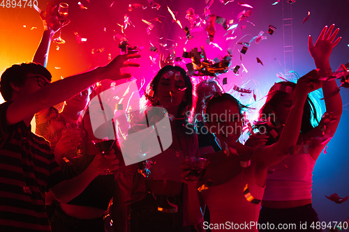 Image of A crowd of people in silhouette raises their hands on dancefloor on neon light background