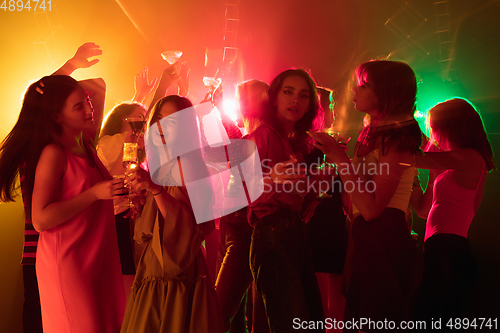 Image of A crowd of people in silhouette raises their hands on dancefloor on neon light background