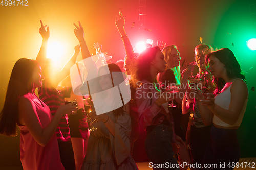 Image of A crowd of people in silhouette raises their hands on dancefloor on neon light background